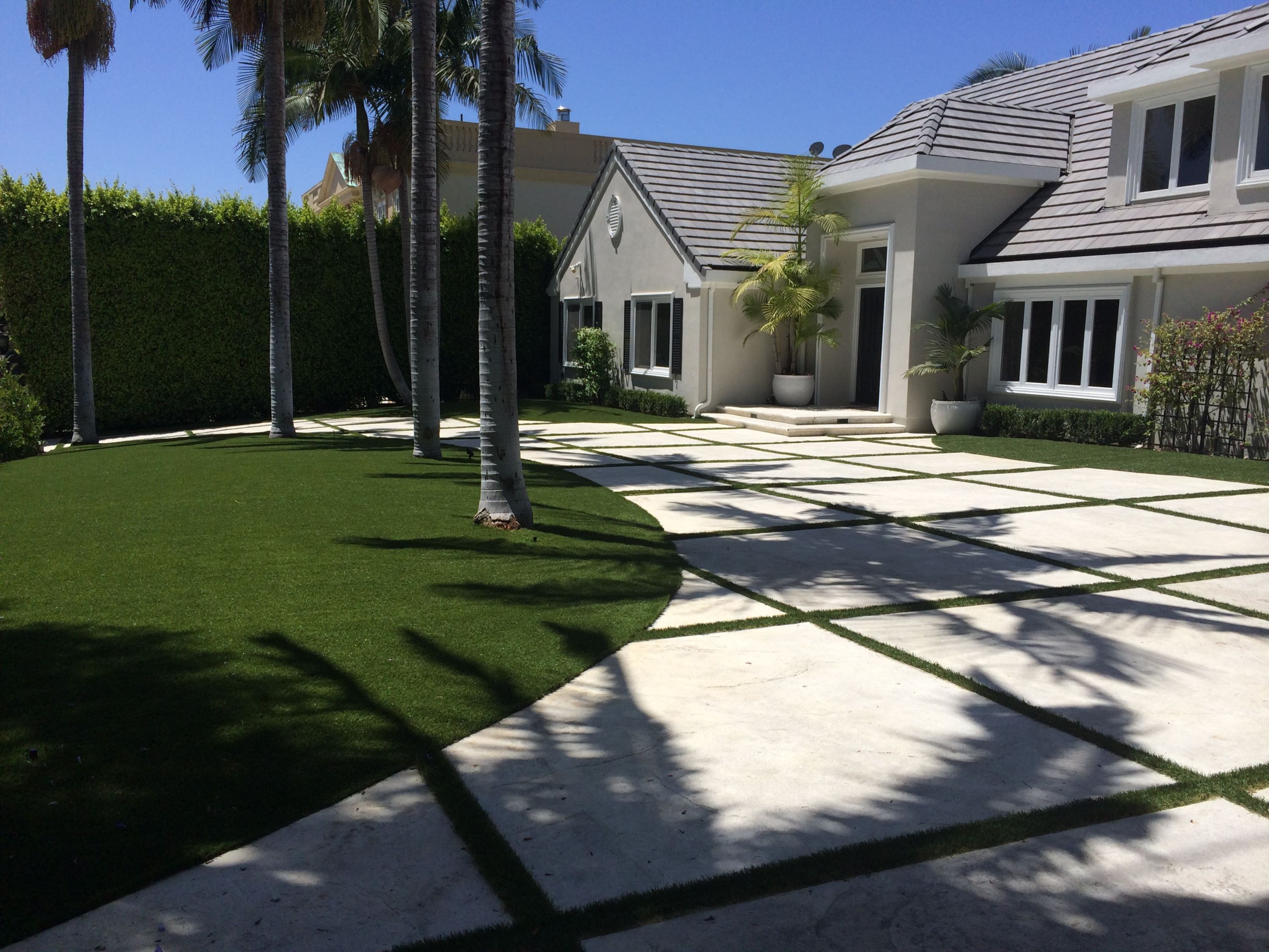 Luxury residential artificial turf installation by Southwest Greens showcasing a modern home with palm trees, custom stone paver driveway, and lush, low-maintenance synthetic lawn.